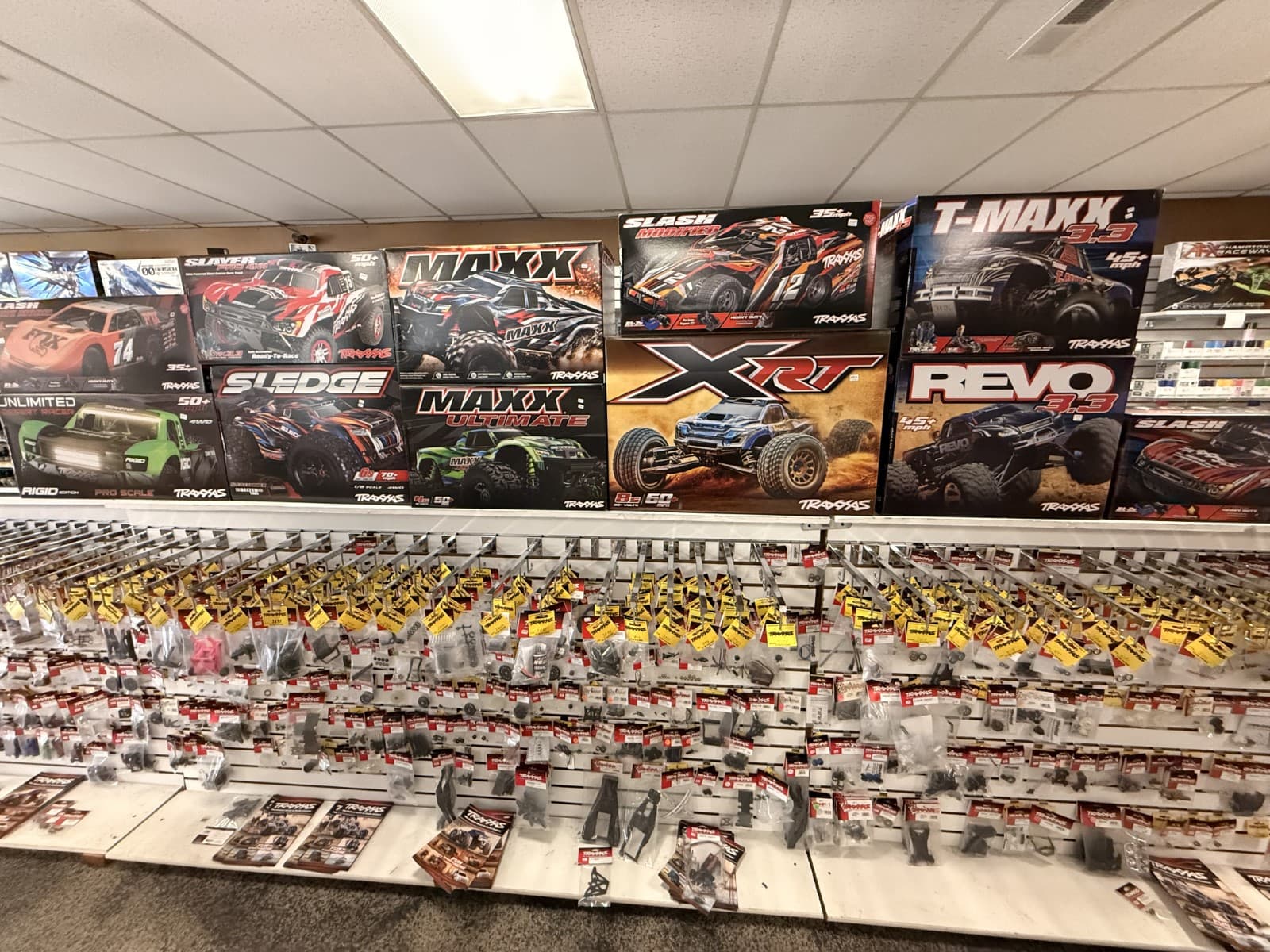 Hobby store wall with Traxxas RC car boxes and rows of hanging replacement parts.